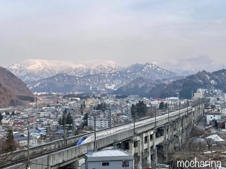 湯沢温泉の街並みと新幹線の写真。遠くに雪化粧の谷川連邦が美しい様子。