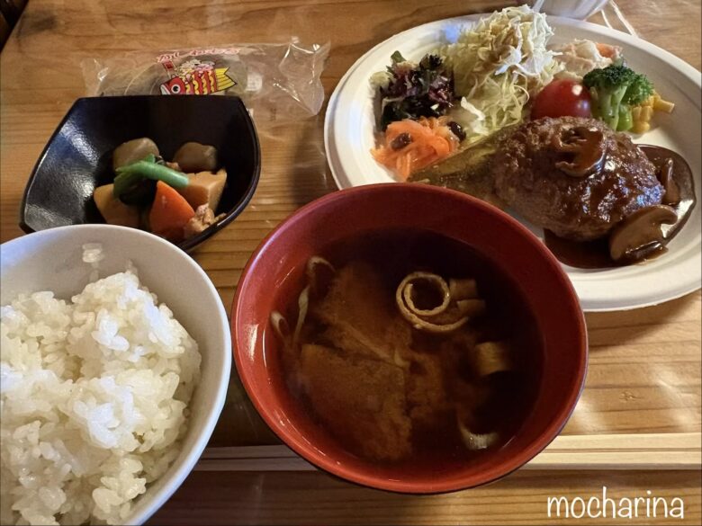山荘の夕食の写真。ハンバーグ、ご飯、カレイの煮付け、煮物、サラダや味噌汁など、品数が多い様子。