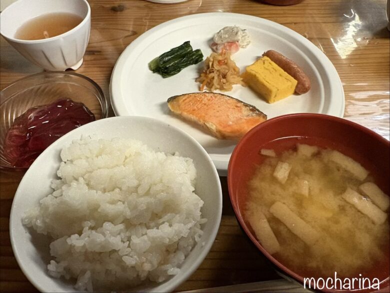 山荘の朝食の写真。焼き鮭、ご飯、玉子焼き、ウィンナー、煮物や味噌汁などが並んでいる様子。
