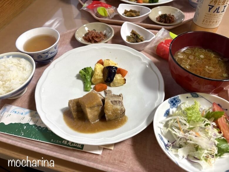 横尾山荘の夕食の写真。煮豚やサラダ、味噌汁、ごはんなど盛りだくさんのおかずが並んでいる様子。