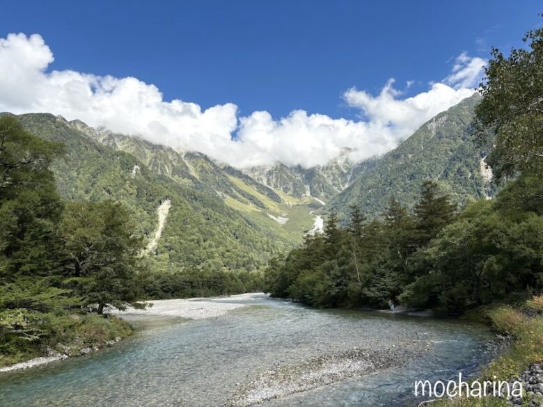 穂高連峰と川の写真。青空と穂高の山並みにかかる雲が美しい様子。
