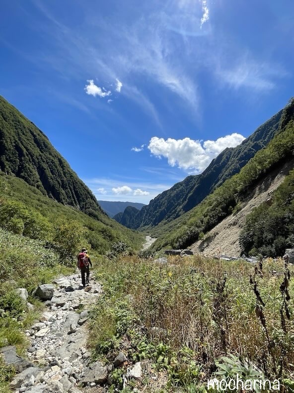槍ヶ岳の登山道を歩く写真。青空と緑の山の谷間を歩く様子。